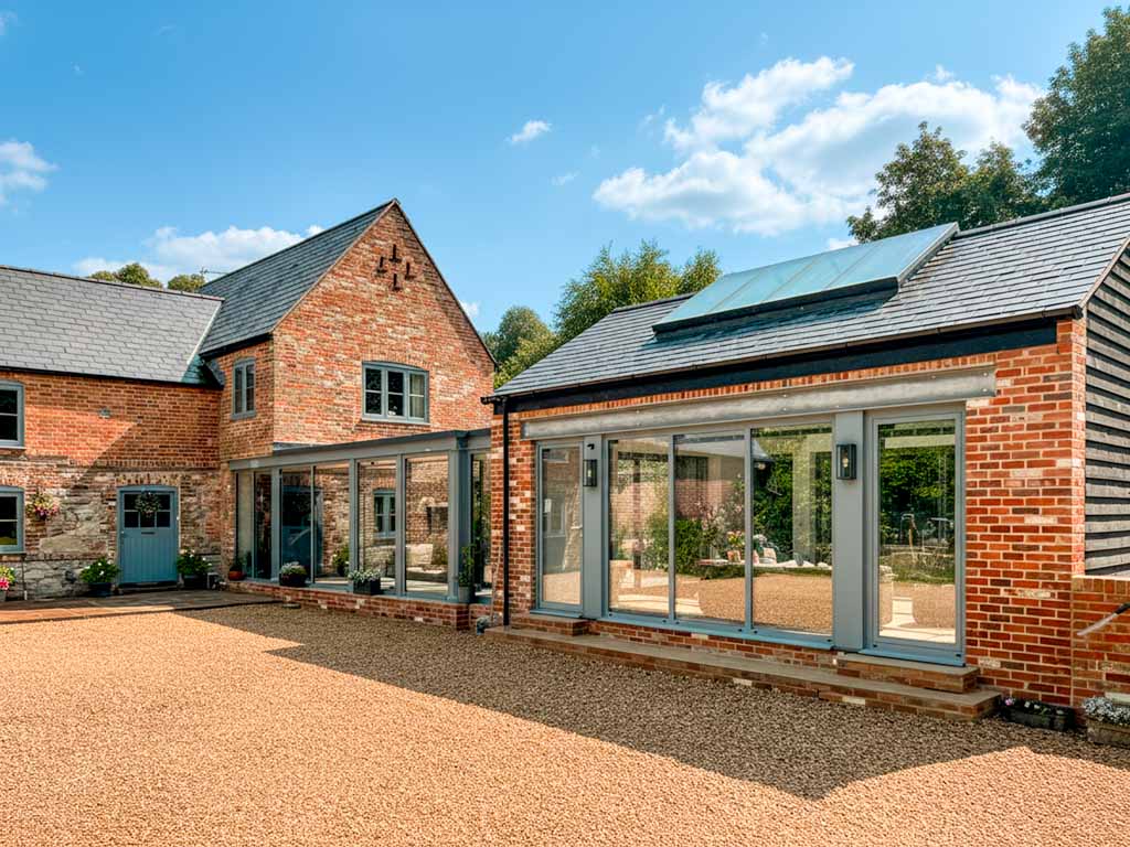 Modern kitchen with white cabinets, a central island with bar stools, and stainless steel appliances. Large glass doors open to a patio, allowing natural light to fill the space. The kitchen feels bright, clean, and inviting.